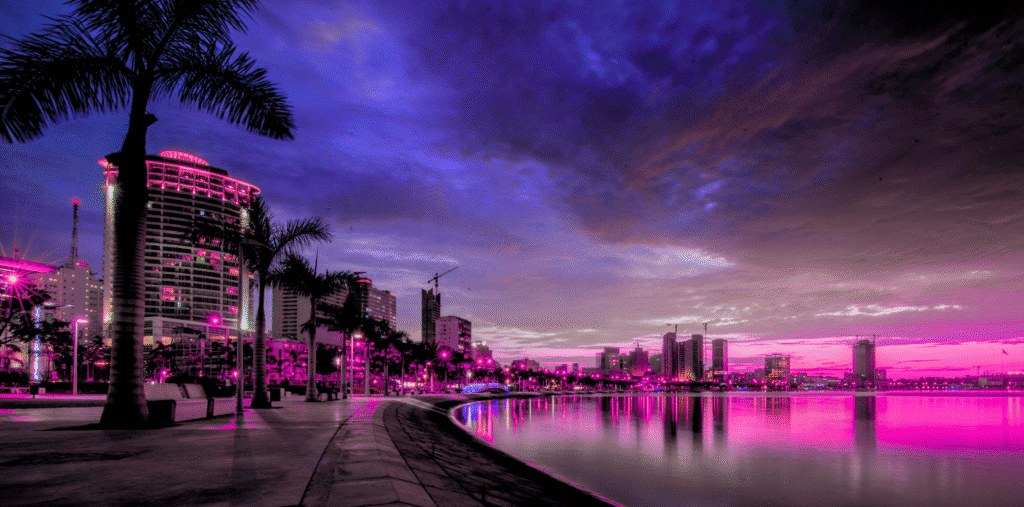 Luanda waterfront skyline at sunset with palm trees and modern buildings.