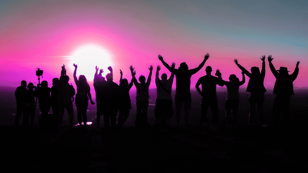 Silhouettes of people celebrating with raised hands during a vibrant sunset.