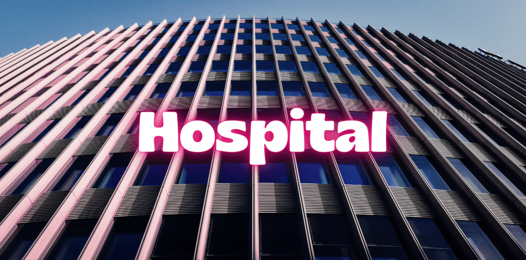 Modern hospital building with the word “Hospital” displayed in bright pink lighting.