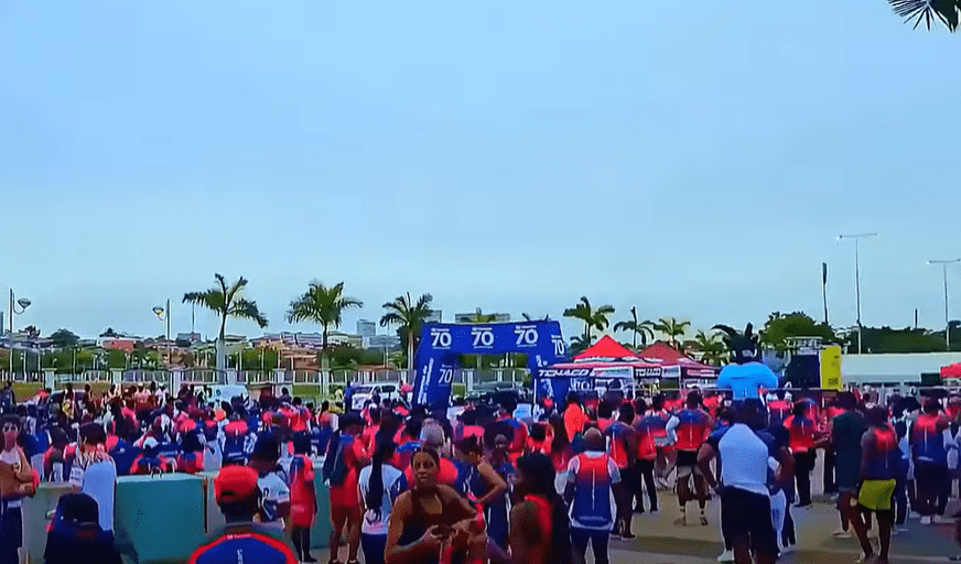 Crowd of participants gathered for a major running event on Luanda’s New Marginal, with palm trees, sponsor tents, and banners in the background under an overcast tropical sky.