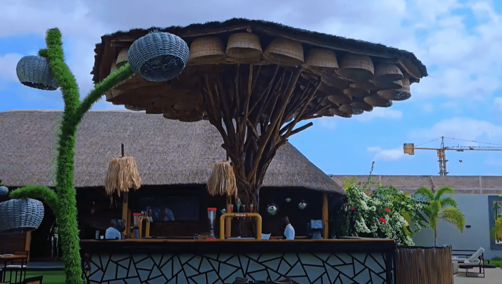 Outdoor bar at Club S Kilamba, featuring a tropical-inspired roof structure made of woven baskets, surrounded by plants and creative lighting fixtures during the day.
