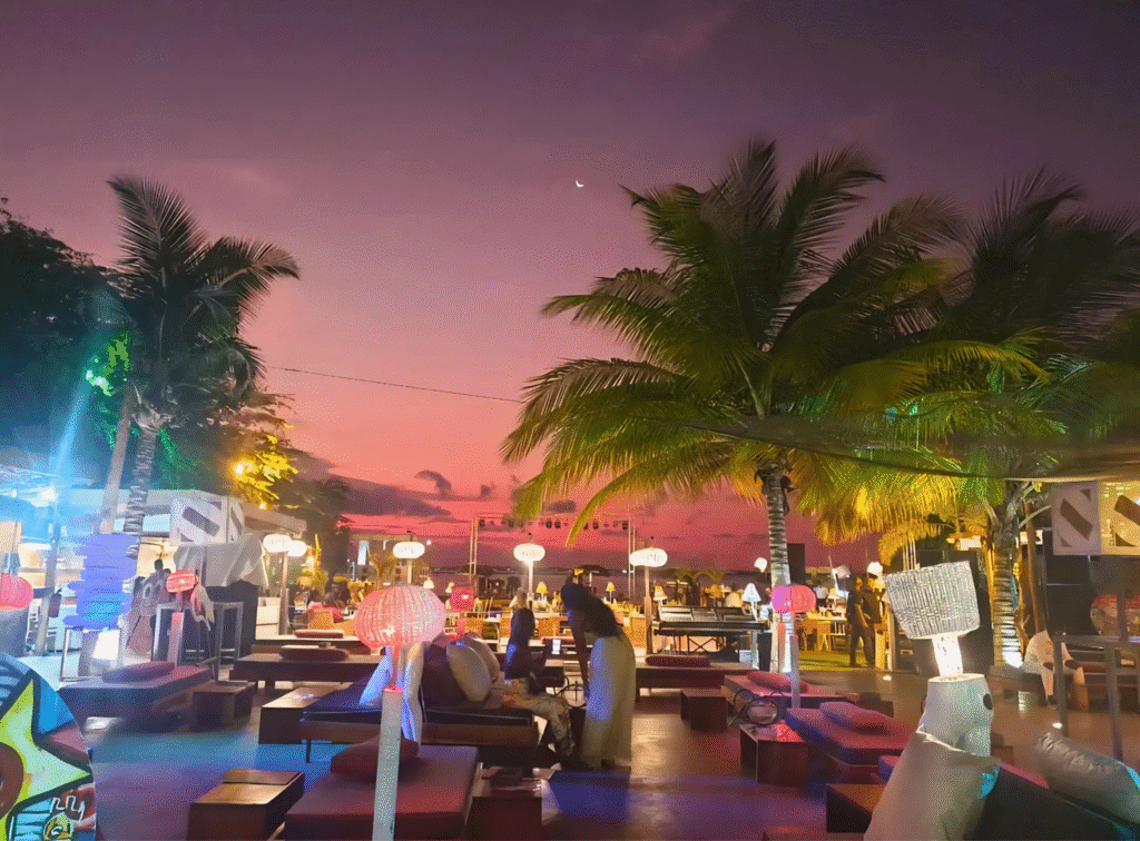 Sunset at Club S with palm trees, lounge seating, and decorative lighting by the sea.