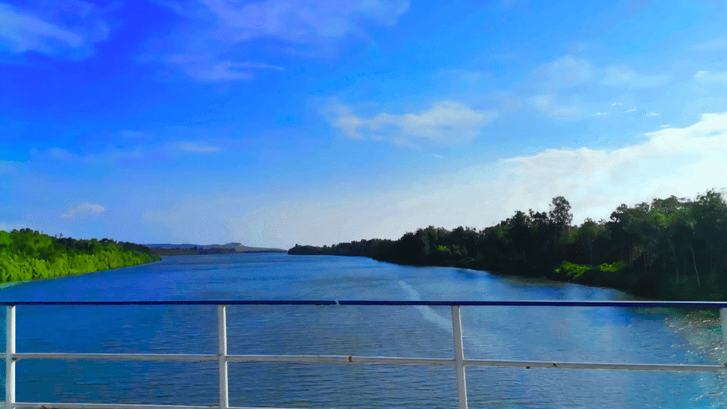 Serene view of the Kwanza River surrounded by lush vegetation, taken from a boat on a sunny day.