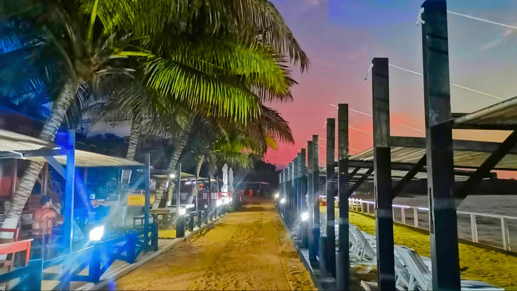 Beachside restaurant at Boutique Lodge Sangano, lit up at dusk with palm trees and sandy paths creating a warm, tropical vibe.