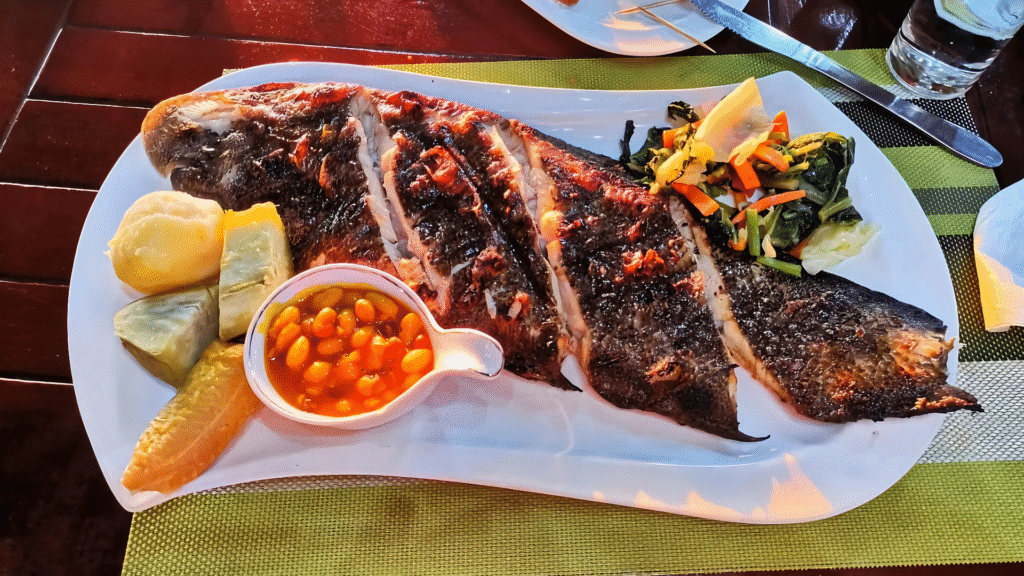 Traditional Angolan dish called "Mufete" with grilled fish, cassava, plantain, sweet potatoes, beans in sauce, and sautรฉed vegetables, served on a white plate.