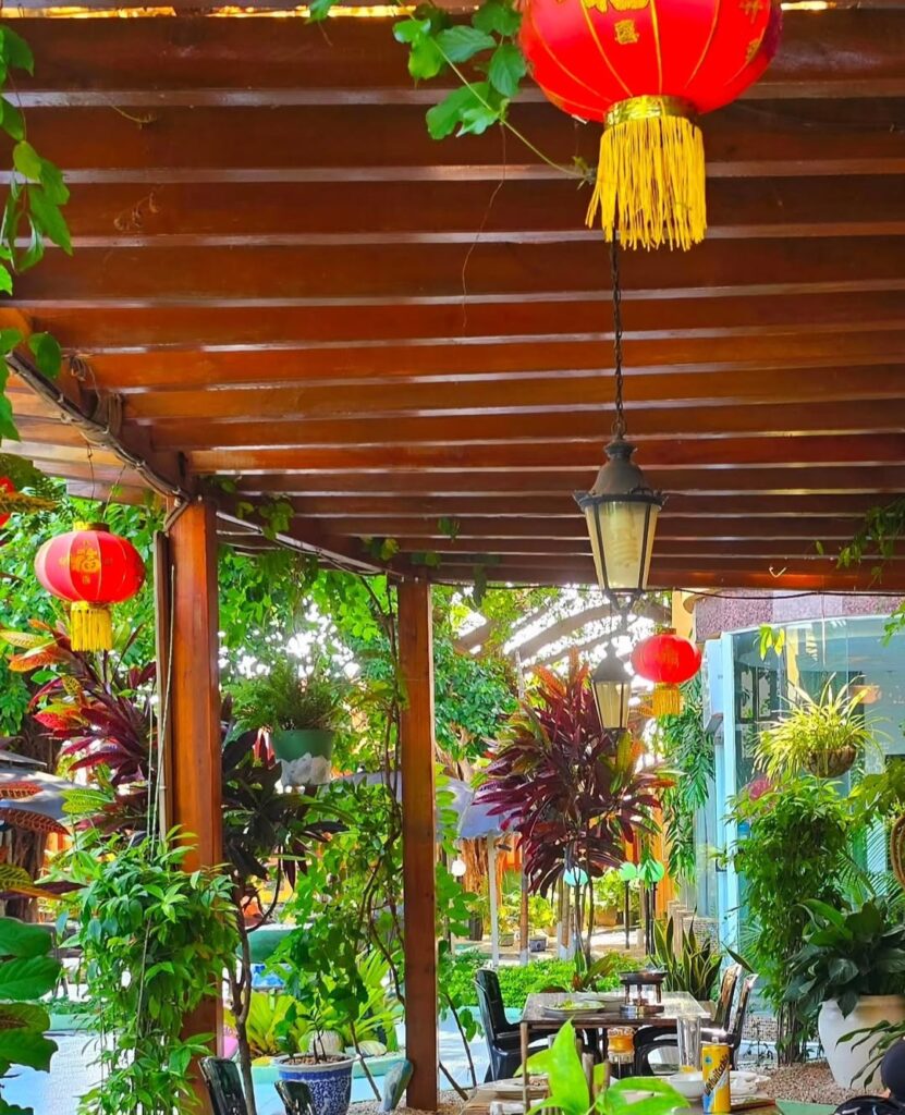 Outdoor seating area at Hao Yun Lai restaurant in Luanda, decorated with traditional red Chinese lanterns and surrounded by lush tropical plants.
