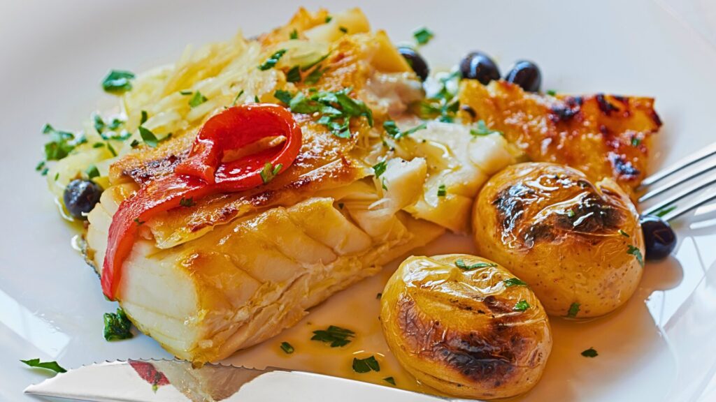 Portuguese grilled codfish topped with red peppers and onions, served with roasted potatoes, olives, and olive oil.