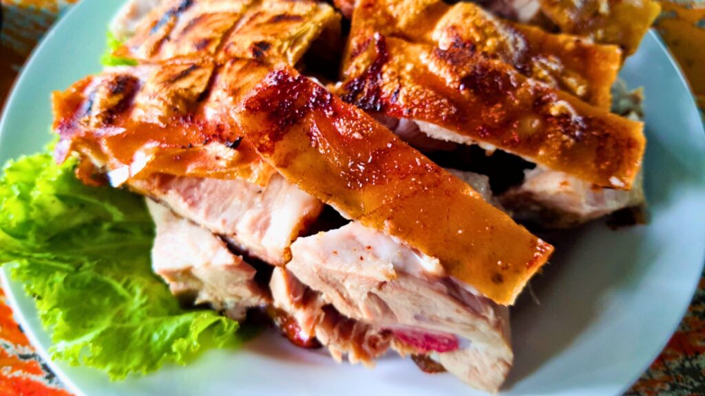Traditional Portuguese roast suckling pig with crispy golden skin and tender meat, served on a bed of lettuce.