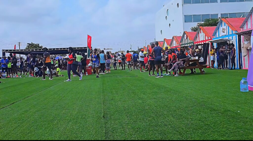Wide view of the Talatona Fitness Fair 2025, with colorful booths on one side and crowds of participants walking, relaxing, and socializing across the green event space.