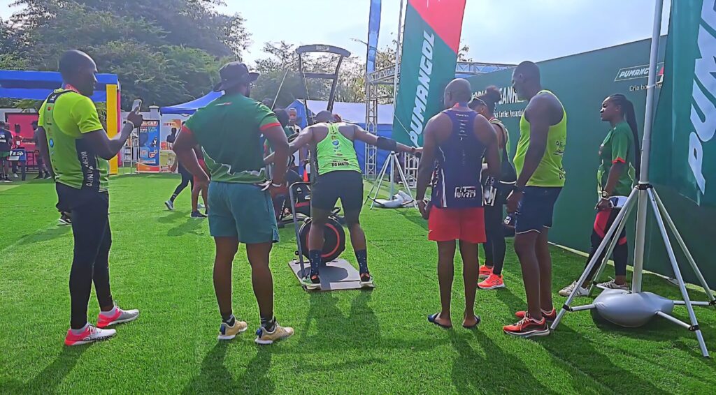 Athletes gathered around a rowing machine challenge booth at the Talatona Fitness Fair 2025 with participants trying equipment under supervision.