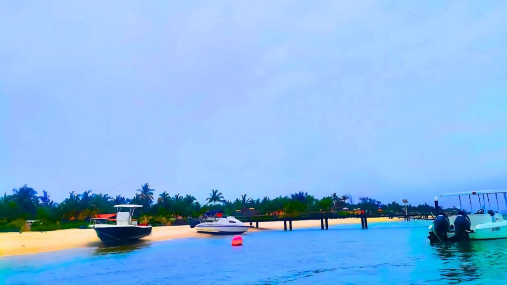 Boats anchored along the sandy shores of Mussulo Island in Angola, with palm trees and calm blue waters creating a tropical paradise.