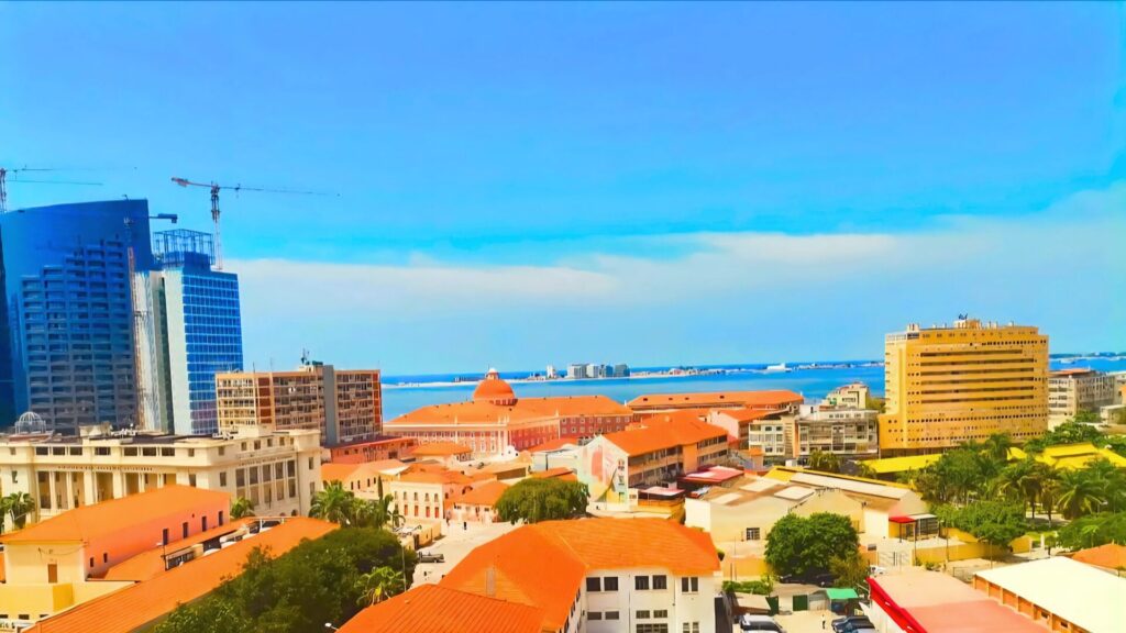 Panoramic view of Luanda with a mix of modern high-rises, colonial buildings with orange rooftops, and the Atlantic Ocean in the background – illustrating daily life in the city