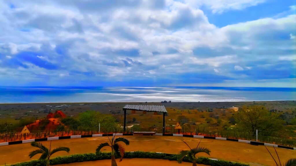 Panoramic view from a viewpoint in Angola overlooking the Atlantic Ocean, with dramatic clouds above, red earth in the foreground and green landscape stretching to the coast.